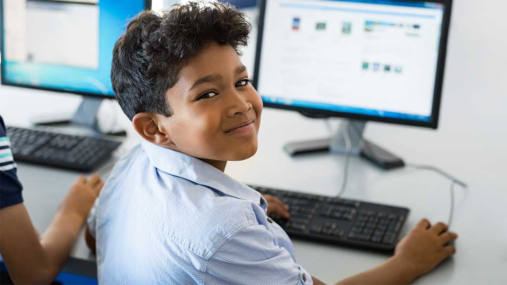 Young happy schoolboy using computer to search internet.